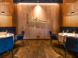 Elegantes Restaurant mit runden Tischen, samtblauen Stühlen und warmem Licht, Schriftzug 'dahoam'