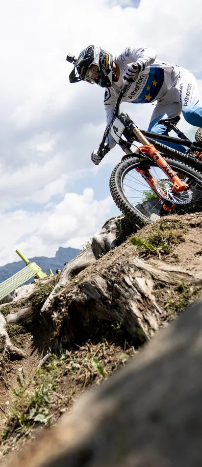 Mountainbike-Rennfahrer fährt einen felsigen Trail bei einem Wettbewerb in den Alpen mit jubelndem Publikum