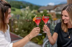 Zwei Frauen stoßen im Freien mit roten Cocktails und Orangenscheiben an