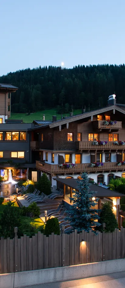 Illuminated alpine hotel with outdoor pool and balconies at sunset