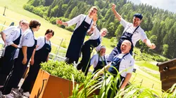 Fröhliches Küchenteam in Arbeitskleidung im sonnigen Garten mit Alpenhintergrund