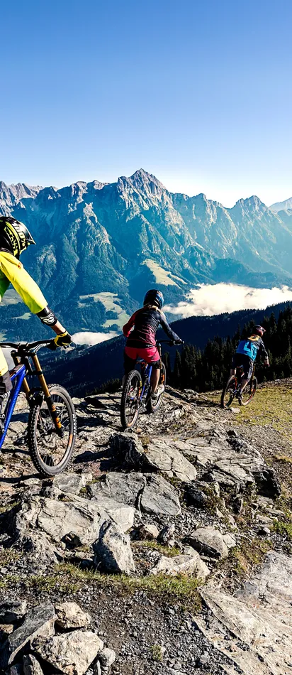 Group of mountain bikers riding downhill on rocky alpine trail with panoramic mountain view