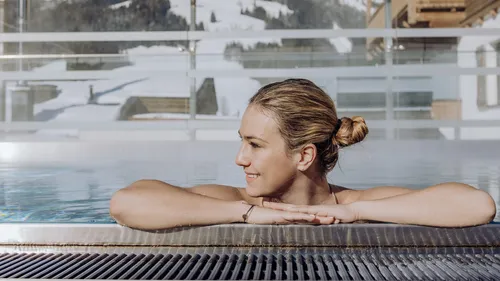Frau entspannt im Outdoor-Spa-Pool mit Blick auf verschneite Berge und blauen Himmel