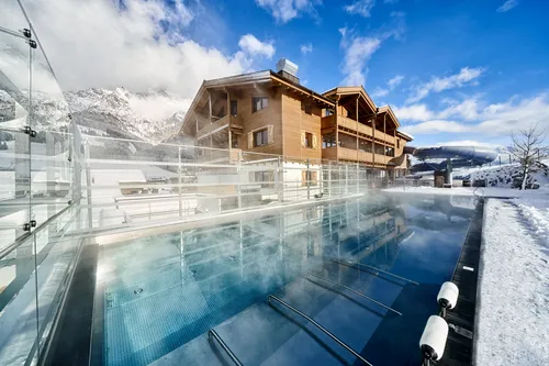Verwarmd buitenzwembad bij skiresort met houten lodge en besneeuwde bergen