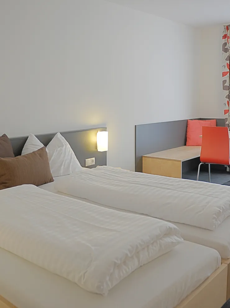 Modernes Hotelzimmer mit Doppelbett, Sitzecke und hellem Tageslicht