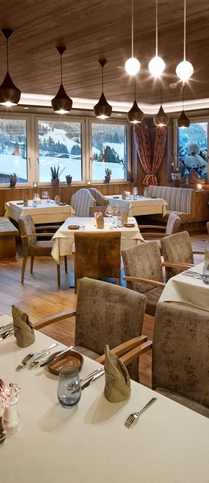 Elegant alpine restaurant interior with set tables and large windows showing snowy mountain view