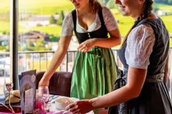 Two women in dirndls setting a table in a mountain-view restaurant