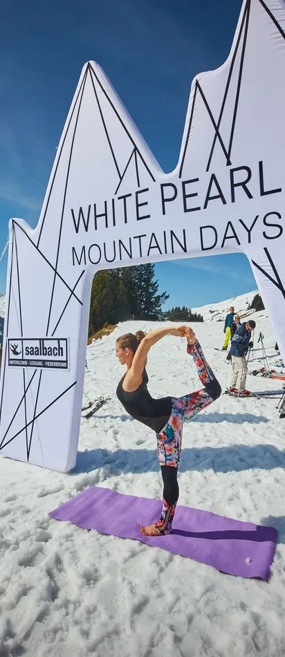 Woman doing yoga on snow at Saalbach White Pearl Mountain Days with skiers in background