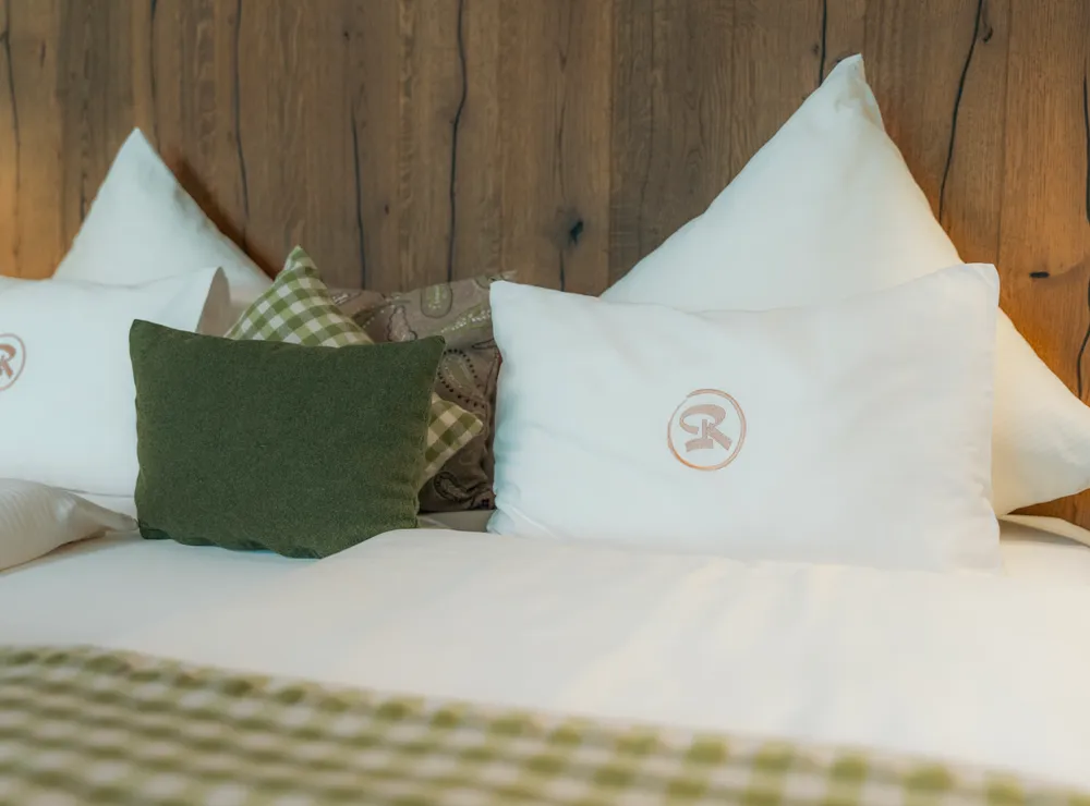 Gemütliches Hotelbett mit weißen Kissen, grünen Polstern und Holzrückwand