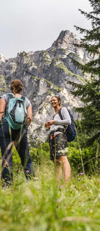 Two women hiking near an information board in a mountain forest landscape
