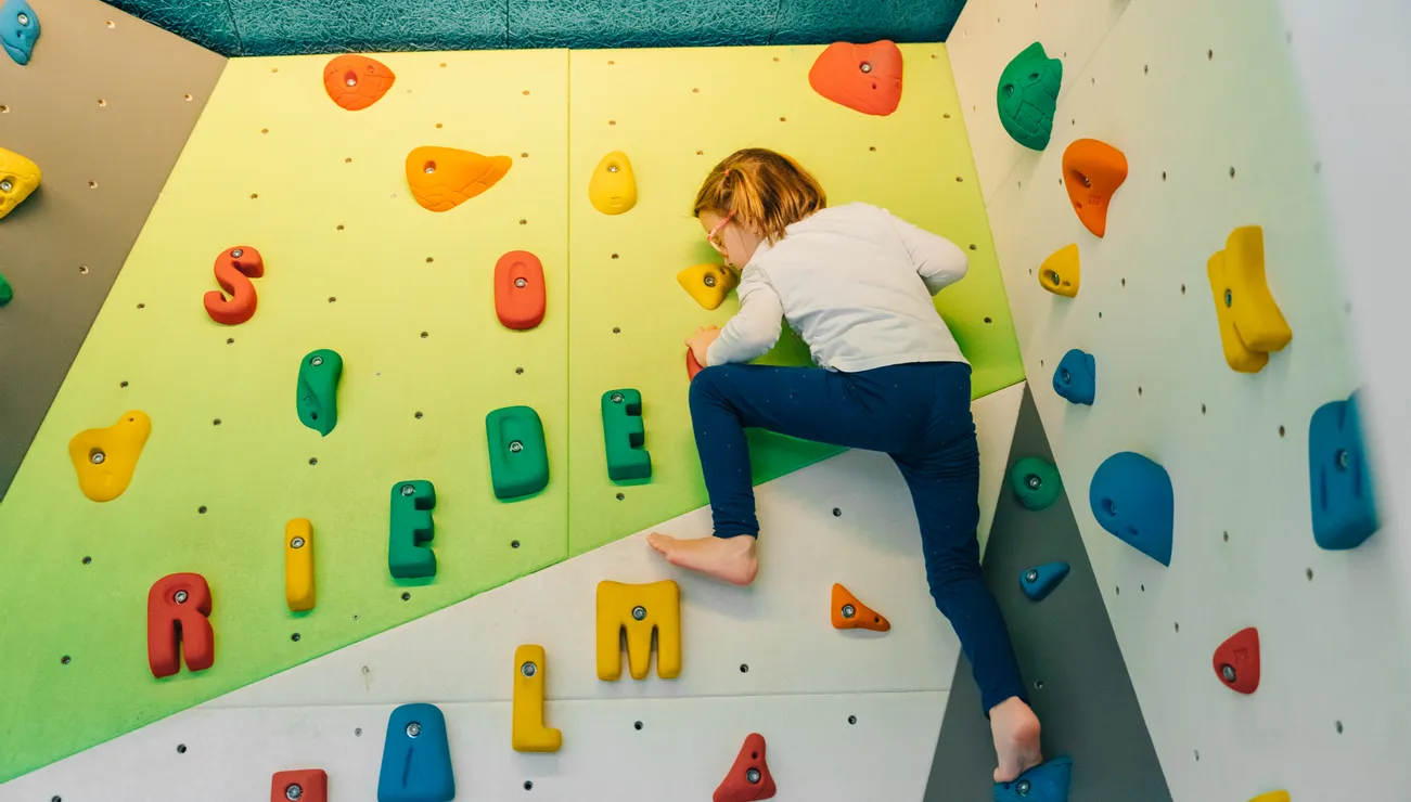 Child climbing indoor bouldering wall with colorful holds shaped like letters
