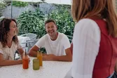 Couple smiling at woman greeting them at outdoor café with drinks on the table
