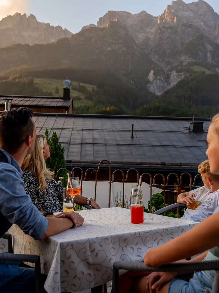 Familie genießt Getränke auf einer Terrasse mit Bergblick bei Sonnenuntergang