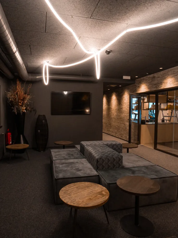 Modern hotel lounge with cozy seating, designer lighting and a view into a gym area