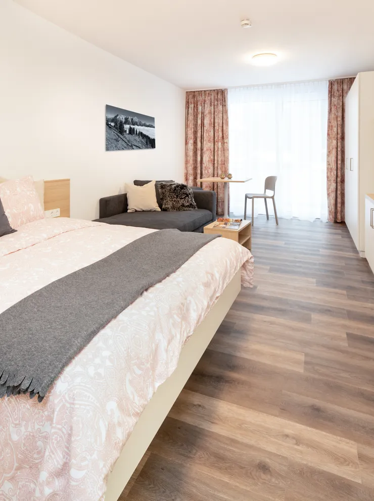 Modernes Hotelzimmer mit Doppelbett, Sofa, TV und Küchenzeile auf Holzboden