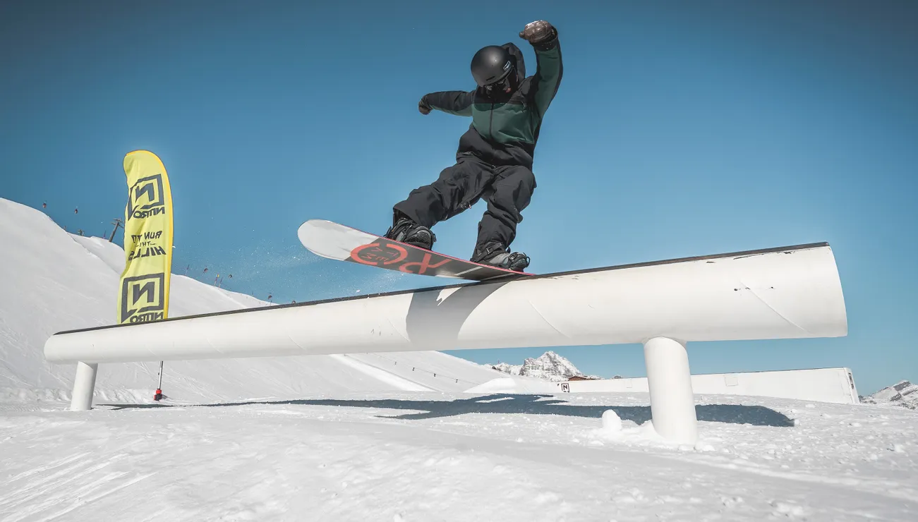 Snowboarder rutscht auf einer Rail im Snowpark bei sonnigem Winterwetter