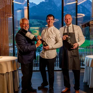 Drei Männer in Gourmetrestaurant mit Weinflaschen und Bergblick im Hintergrund