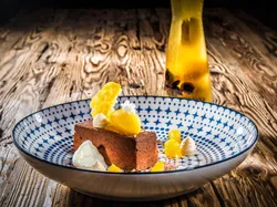 Chocolate dessert with mango and cream dollops in decorative bowl on rustic wooden table
