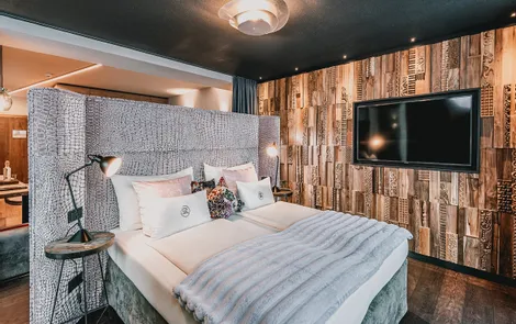Modernes Hotelzimmer mit gepolstertem Bettkopfteil, Holzwand und großem Flachbildfernseher