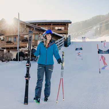 Frau in Skikleidung mit Skiern vor Chalet im sonnigen Skigebiet