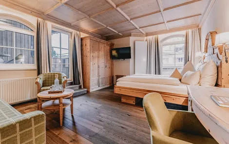 Gemütliches Hotelzimmer mit Holzmöbeln, Doppelbett, Sitzecke und großen Fenstern