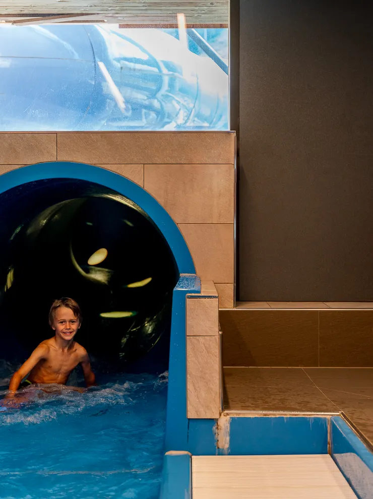 Smiling boy exits indoor waterslide into shallow blue pool in water park