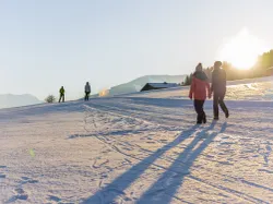Menschen beim Winterwandern bei Sonnenuntergang in einer verschneiten Berglandschaft