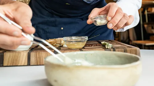 Chef plating gourmet dish with tweezers in a modern restaurant kitchen