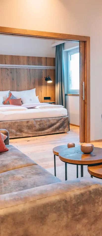 Modern hotel suite with cozy lounge area, round tables and view into the bedroom