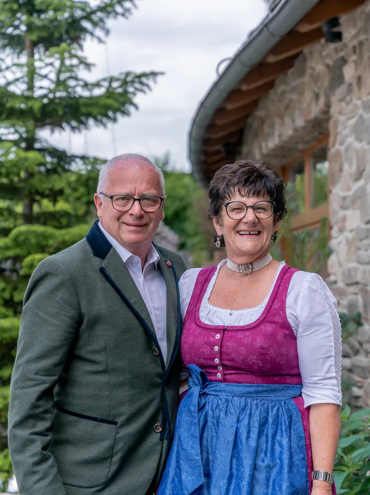 Lächelndes Paar in traditioneller bayerischer Kleidung vor einem Steinhaus im Freien