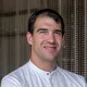 Male chef in white uniform with Riederalm logo standing in front of decorative curtain