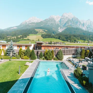 Outdoor swimming pool with sun loungers at hotel resort overlooking alpine mountains