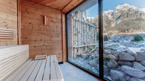 Wooden sauna with panoramic window overlooking snowy alpine mountain landscape