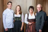 Vier Personen in traditioneller österreichischer Kleidung und moderner Kochuniform posieren gemeinsam