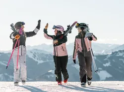 Three women in ski gear high-five on a snowy mountain with skis and poles