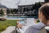 Woman in bathrobe reading a spa brochure by an outdoor pool at a wellness resort
