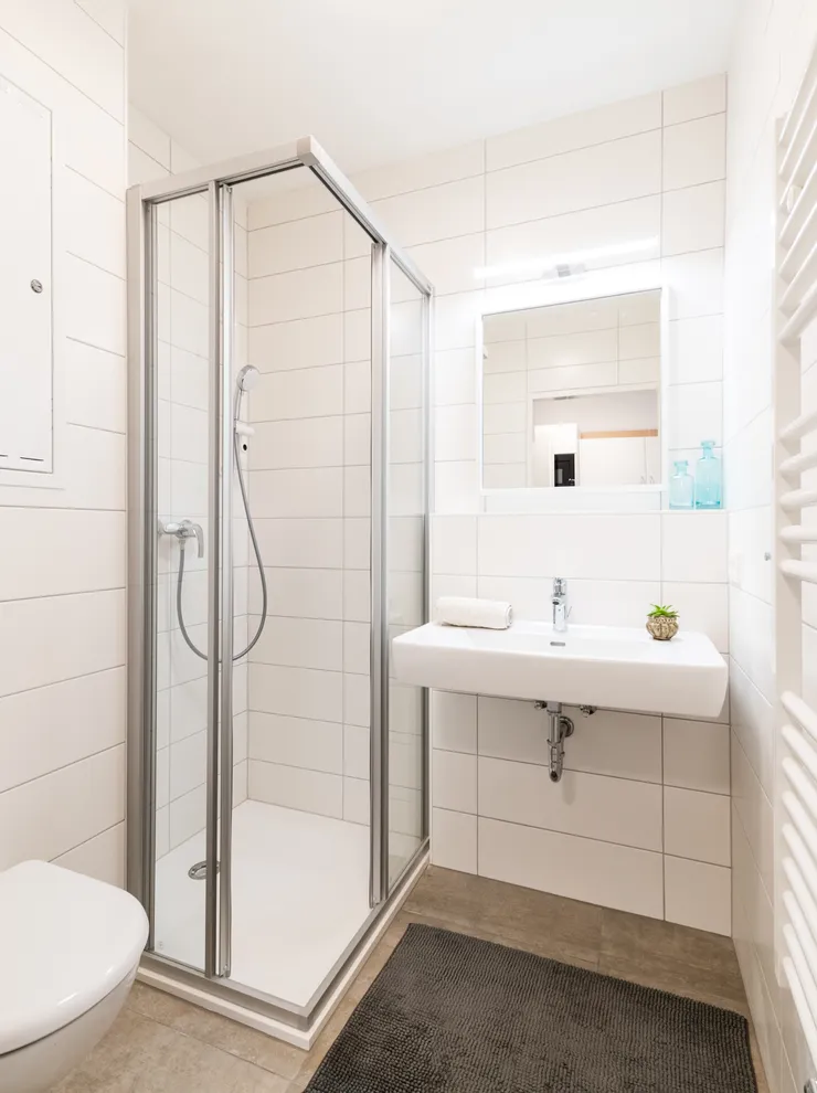 Modernes weiß gefliestes Badezimmer mit Dusche, Wandtoilette und Waschbecken