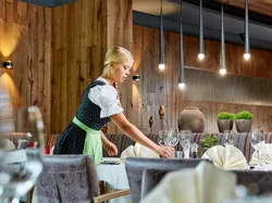 Kellnerin im Dirndl deckt Tisch in gehobenem rustikalem Restaurant
