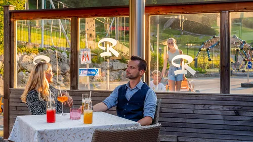Couple enjoying colorful drinks at outdoor restaurant near playground during sunset