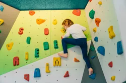Kind klettert an Indoor-Boulderwand mit bunten Griffen in Buchstabenform