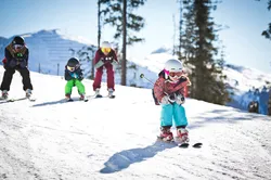 Children skiing downhill in a line on a sunny snowy mountain slope