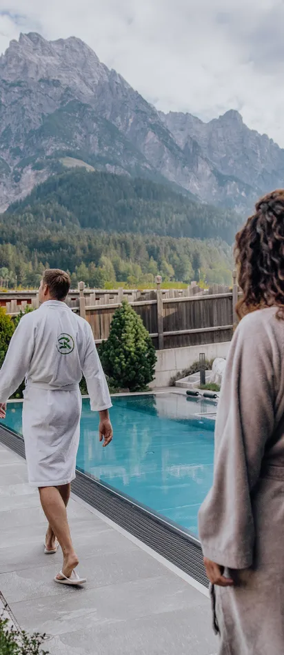 Couple in bathrobes walking by outdoor spa pool with Alpine mountain view