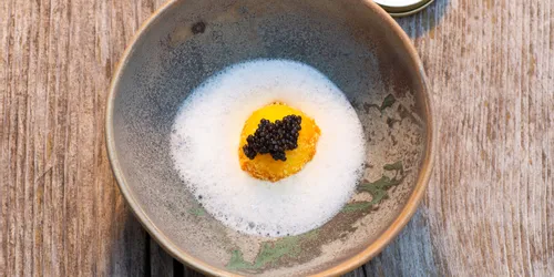 Gourmetgericht mit Kaviar und Schaumsauce auf rustikalem Holztisch