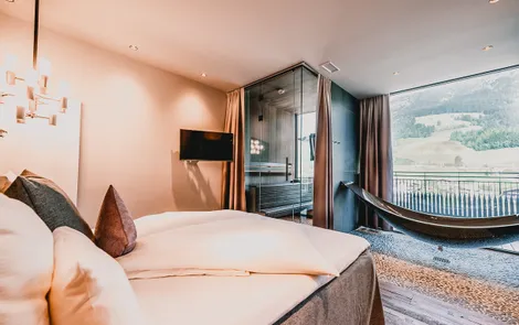 Modern hotel room with double bed, hammock lounger, sauna and mountain view