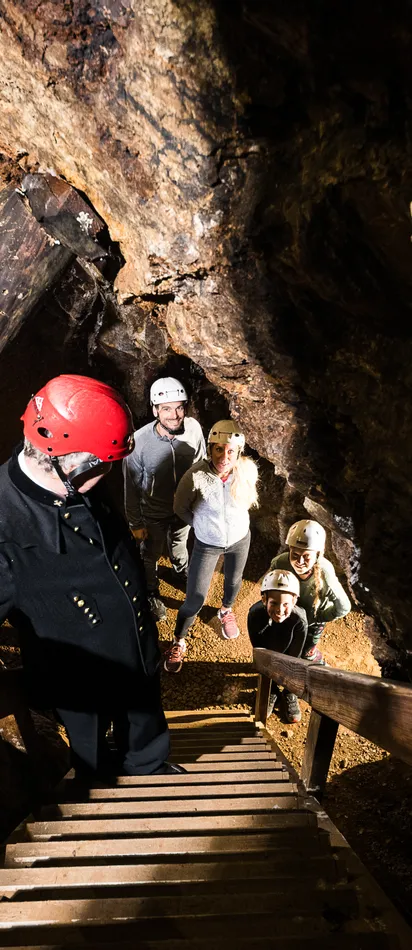 Tour guide leading visitors wearing helmets inside an illuminated mine tunnel