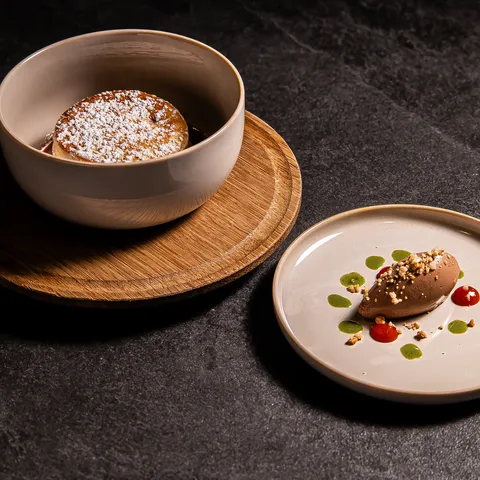 Schokoladensoufflé mit Puderzucker und Mousse mit Soßentropfen auf dunklem Steinuntergrund