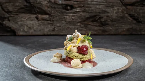 Gourmet dessert with sponge cake, cherry, cream, and edible flowers on a ceramic plate