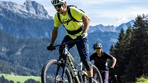 Two mountain bikers riding uphill on a trail in the Alps on a sunny day
