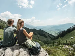 Wanderer rasten auf einem Felsen mit Panoramablick auf Alpental und Berge