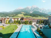 Außenpool mit Liegestühlen vor Alpenkulisse in sonniger Hotelanlage